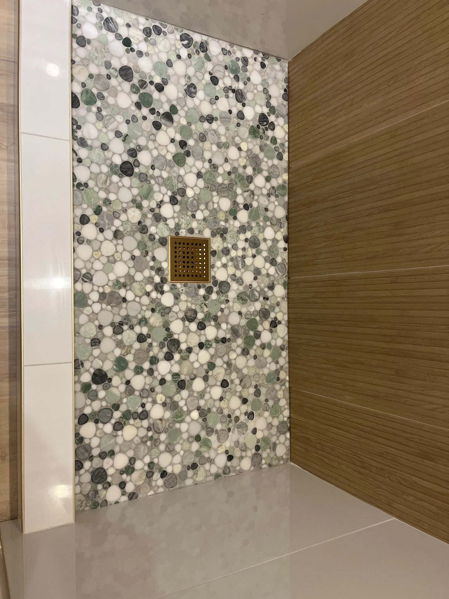 Custom bathroom shower with green and gray pebble mosaic accent wall and gold drain
