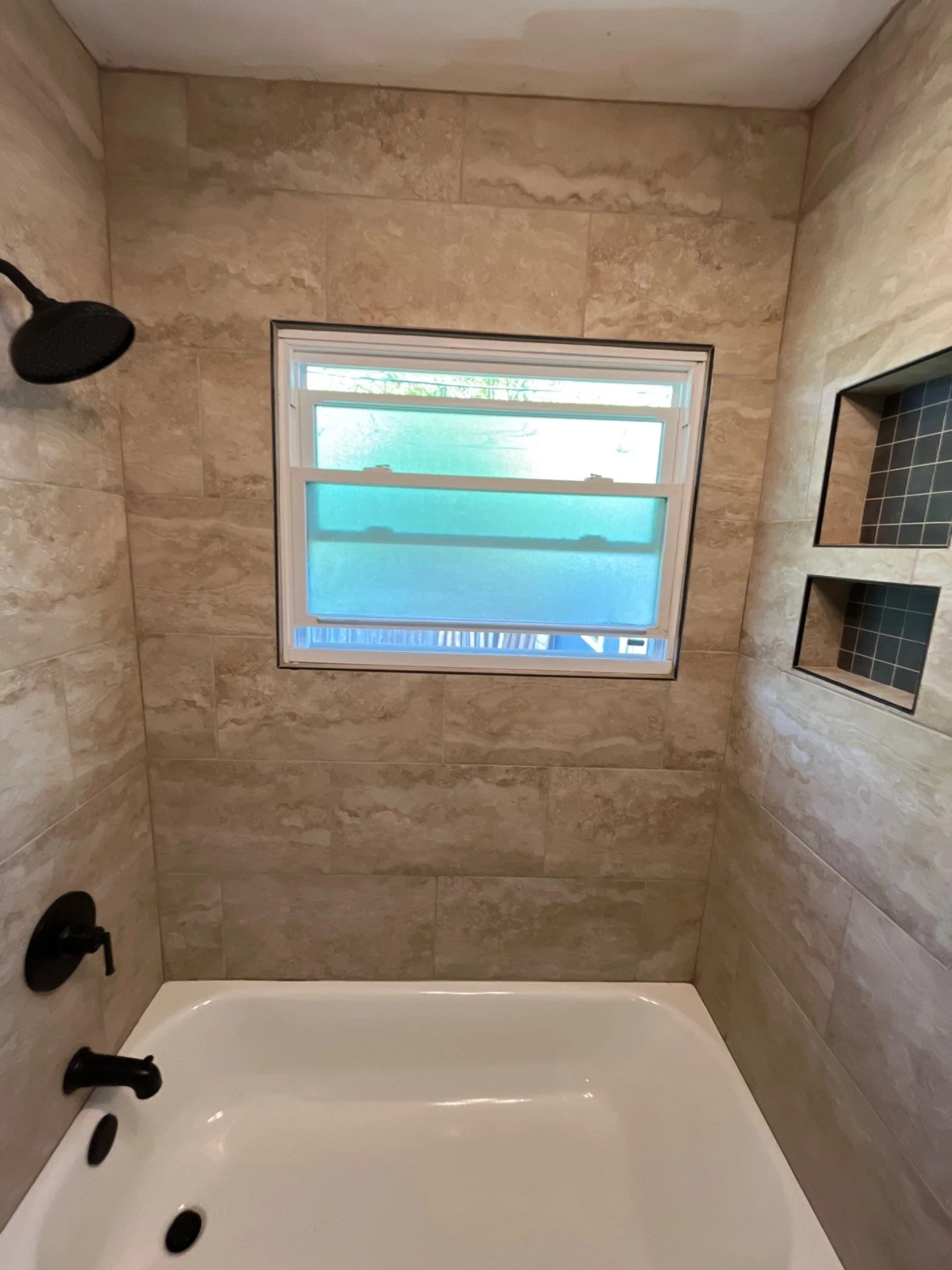 Travertine tile tub surround with built-in niche and modern black fixtures
