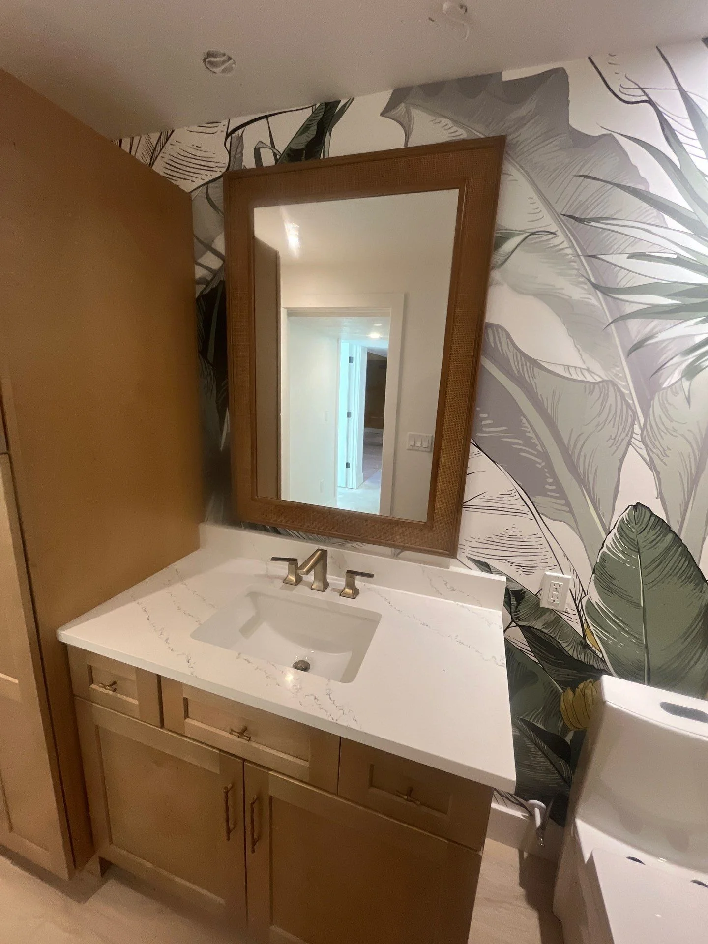 Custom bathroom vanity with quartz countertop, framed mirror, and tropical wallpaper accent