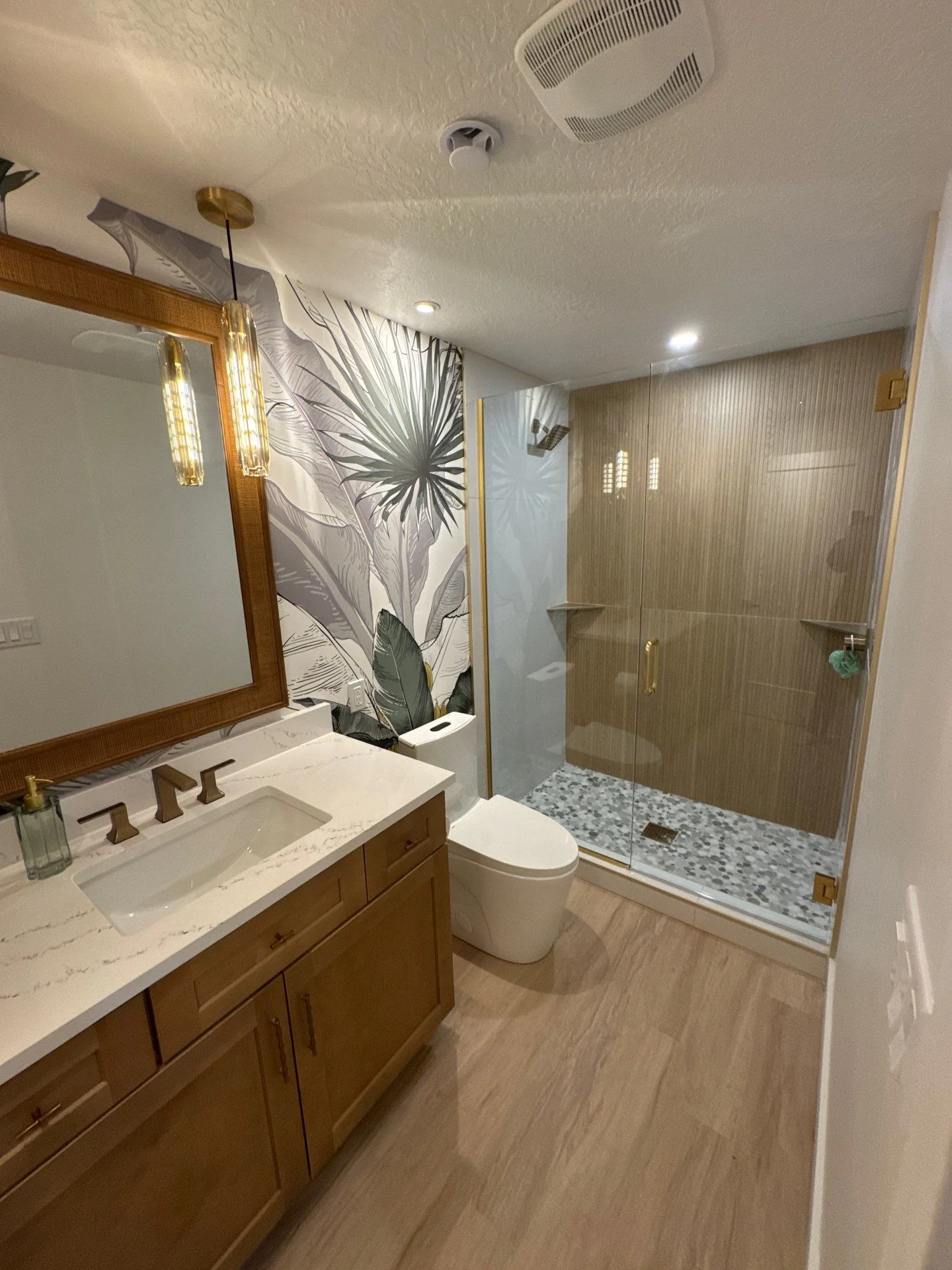 Finished bathroom remodel with custom vanity, framed mirror, glass shower enclosure, and tropical wallpaper accent