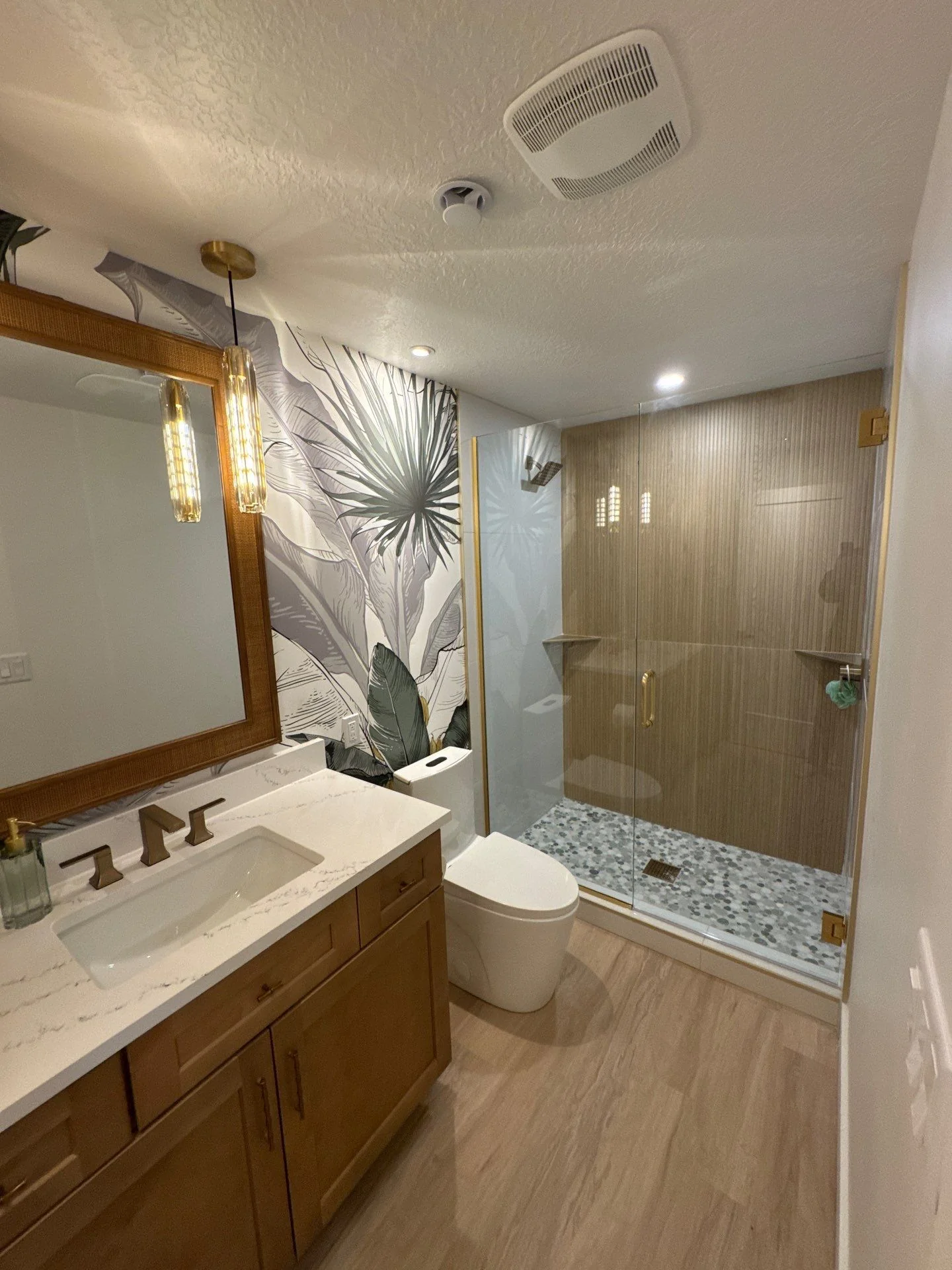 Finished bathroom showing wood-look slat tile shower wall, glass enclosure, and pebble mosaic floor
